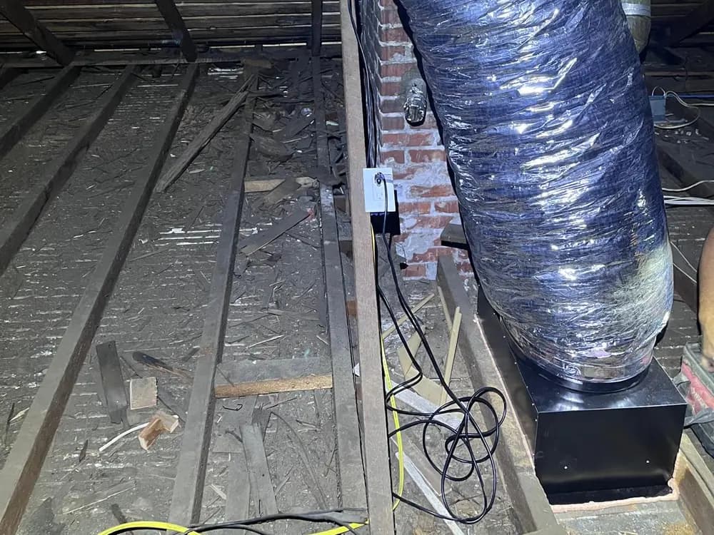 Attic fan housing mounted to the framing and connected to a run of insulated flexible duct.