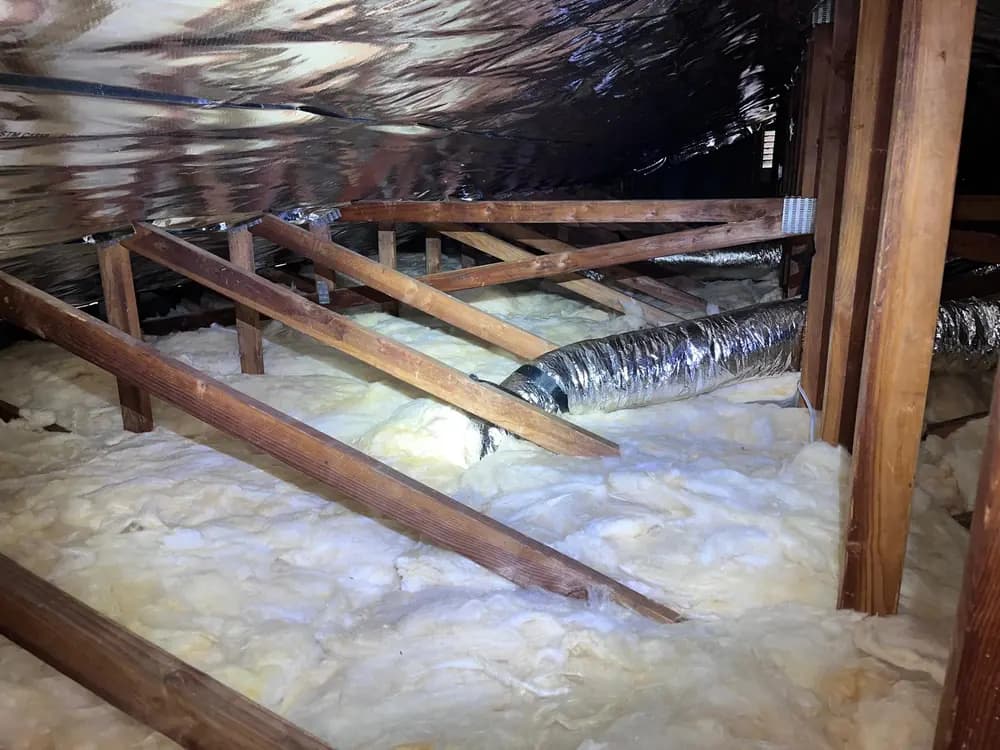 Attic floor covered with an even layer of insulation, with ductwork routed above it and a radiant barrier at the roof line.