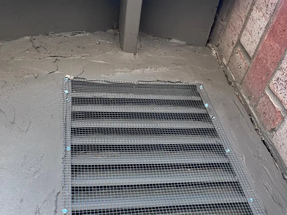 Foundation vent covered with galvanized mesh, fastened at the edges and mortared into the surrounding wall.