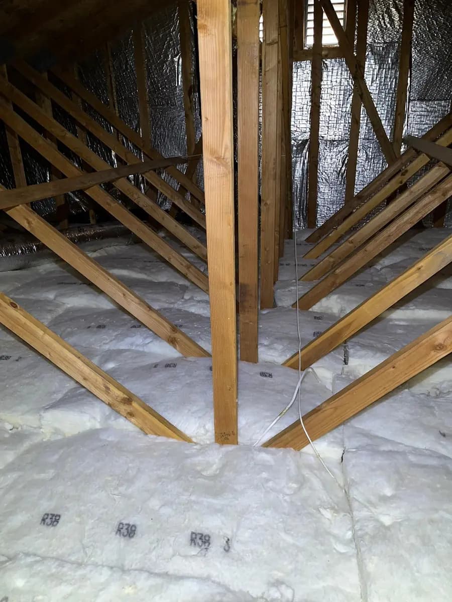 Attic floor with new batt insulation laid evenly between the joists and a radiant barrier fitted along the rafters above.